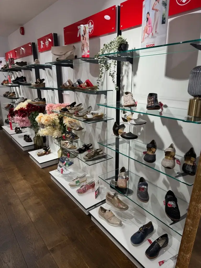 A display of various stylish shoes on glass shelves, with decorative flowers and promotional posters in a retail setting.