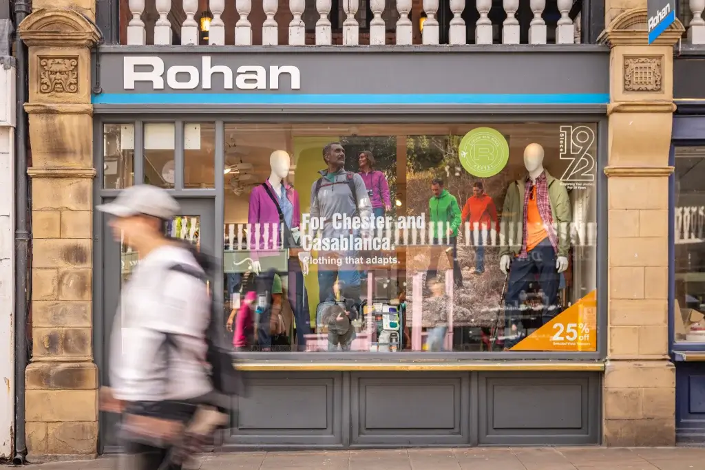 The Rohan store window showcases outdoor clothing with mannequins dressed in colorful attire, promoting adaptability and a seasonal sale.