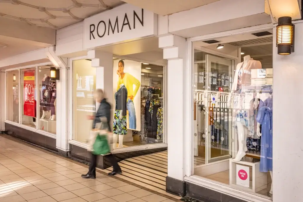 A storefront of Roman with a variety of women's clothing displayed in the windows, including dresses and sales signage.