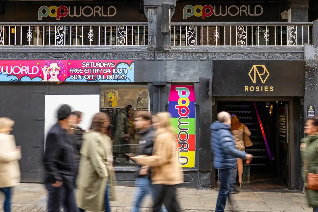 A busy street scene featuring a vibrant bar called "Popworld," promoting drink deals, alongside a sleek entrance to "Rosies."