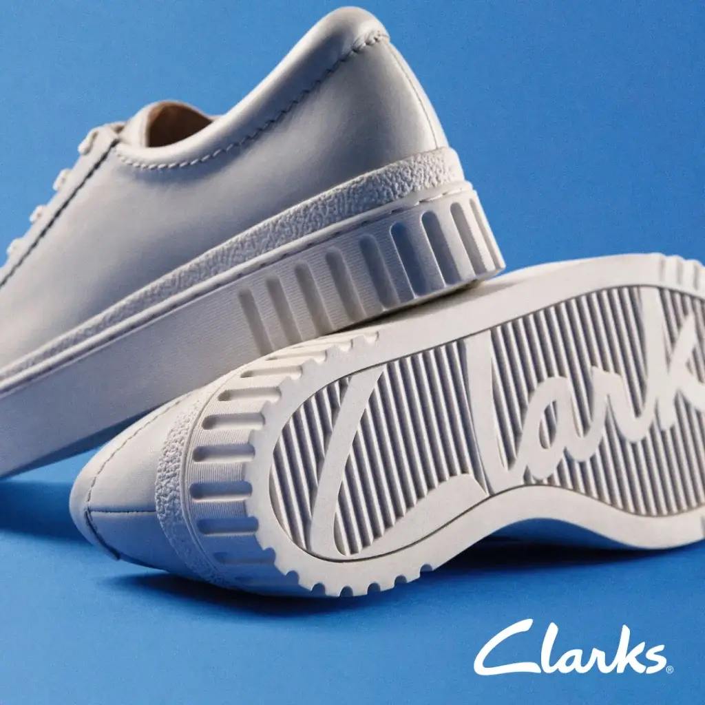 A pair of white Clarks sneakers with textured soles, set against a vibrant blue background.