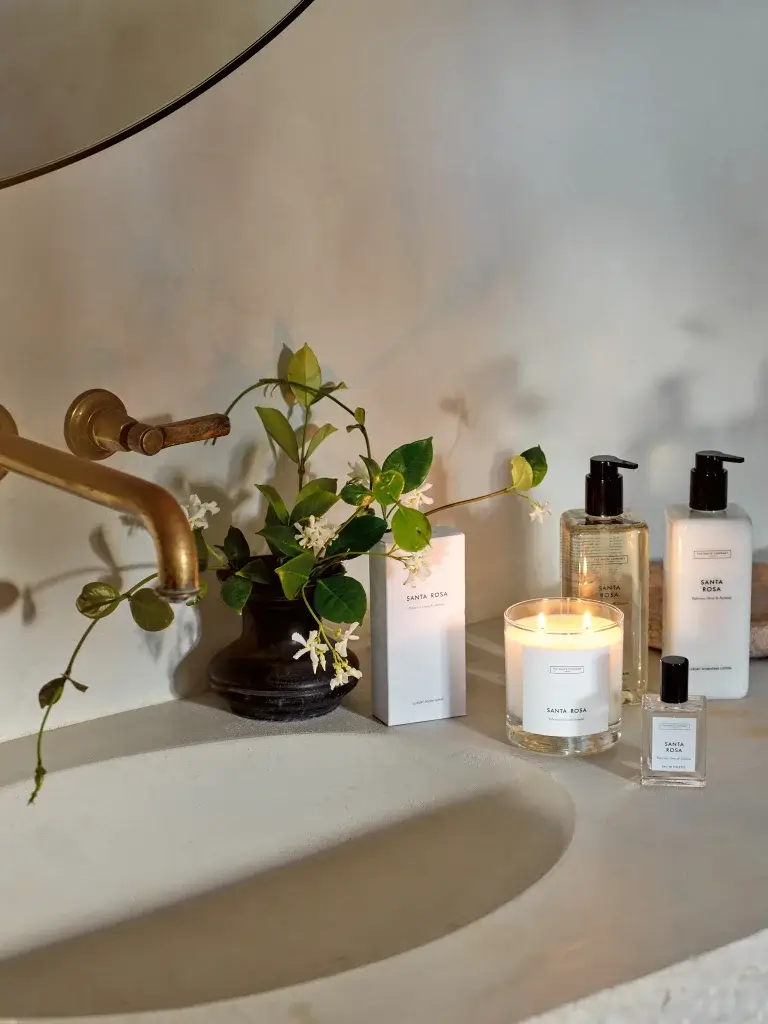A bathroom sink adorned with a lit candle, elegant skincare products, and a small vase of greenery, reflecting a serene ambiance.