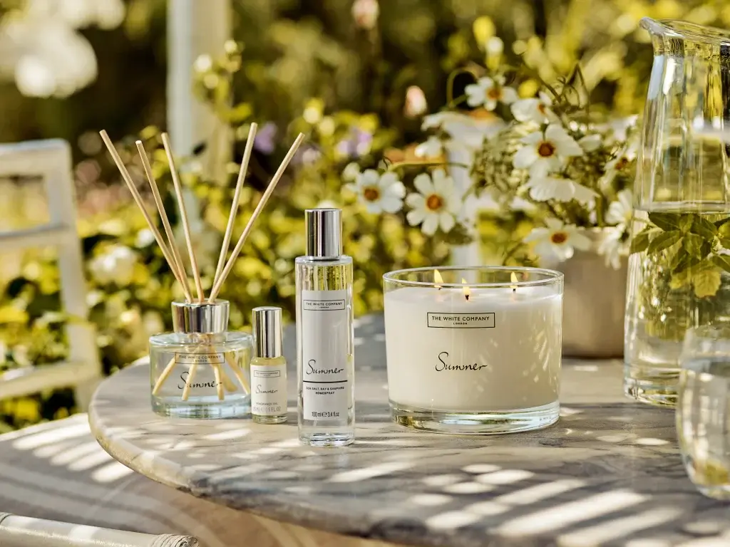 A serene outdoor setting featuring scented candles, reed diffusers, and floral arrangements on a rustic table.