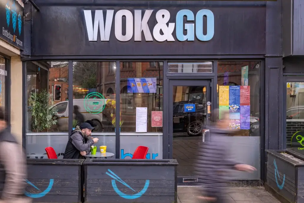 A vibrant Asian eatery named WOK&GO features outdoor seating, colorful menus, and a lively street scene bustling with pedestrians.