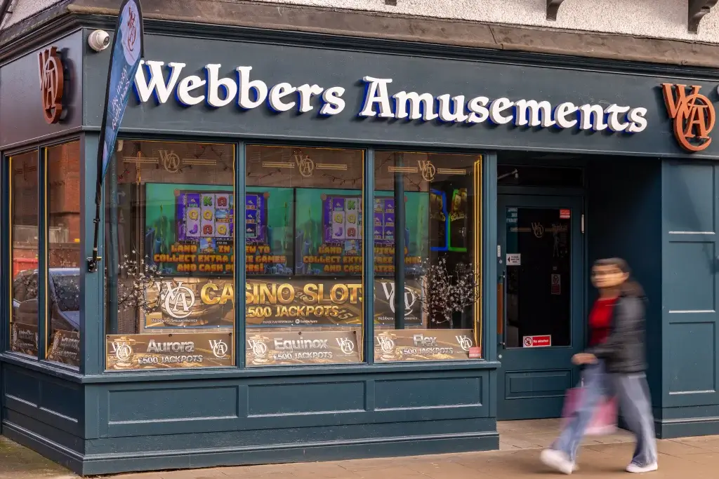 Webbers Amusements storefront showcasing casino slot machines and colorful promotions, with a person walking by.