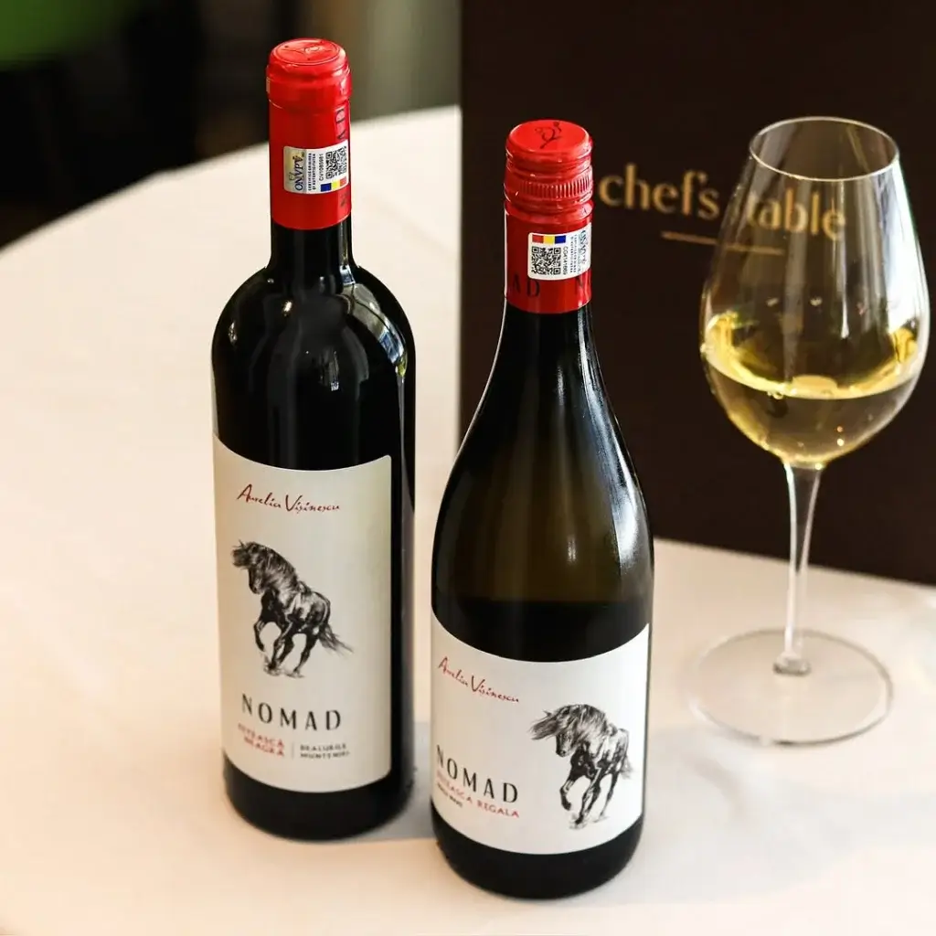 Two bottles of Nomad wine, one red and one white, beside a glass of white wine on a table with a brown menu in the background.