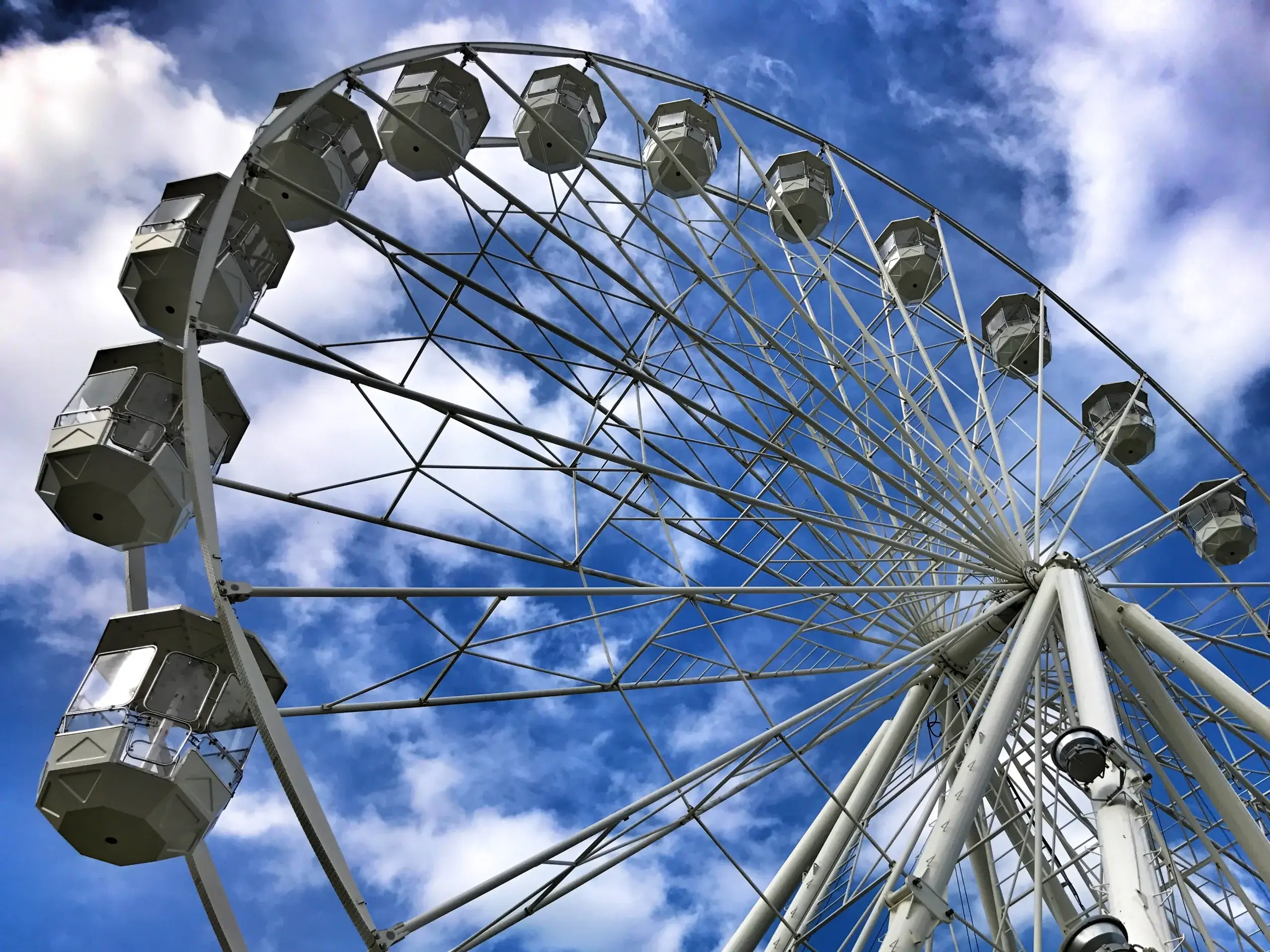 A towering white Ferris wheel against a bright blue sky with fluffy clouds, showcasing its round structure and glass cabins.