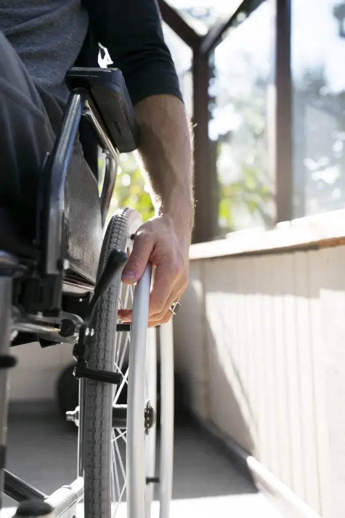 A close-up of a hand gripping the wheel of a wheelchair, emphasizing movement and independence in a sunlit room.