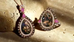 A luxurious pink gemstone necklace and matching ring set on a textured stone surface, featuring intricate designs and sparkling diamonds.