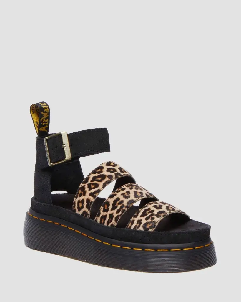 Black platform sandals with leopard print straps and an adjustable ankle buckle, featuring Dr. Martens signature yellow tag.