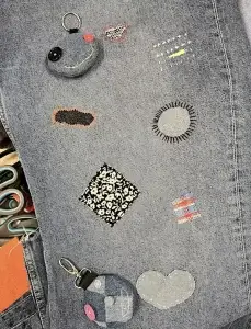 A denim fabric with various stitched patches, including a smiley face, hearts, a flower pattern, and colorful designs.