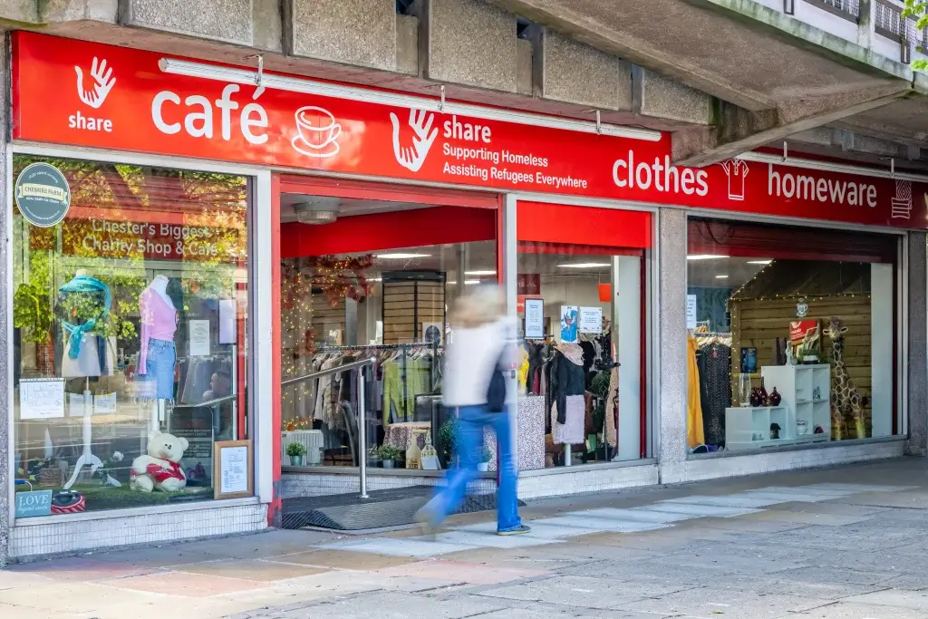 A charity shop and café with a vibrant red sign, showcasing clothing displays and a stuffed teddy bear in the window.