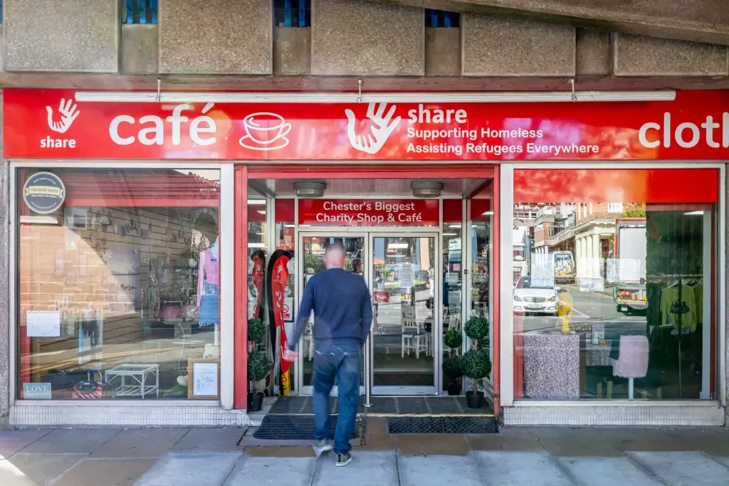 A man exits a charity shop and café named "Share," which supports the homeless and refugees, located in Chester.