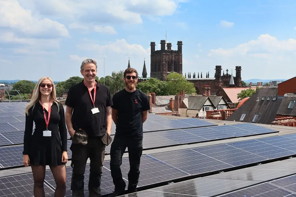 Storyhouse roof with new solar panels installed across, three people stand facing camera with chester cathedral in the background
