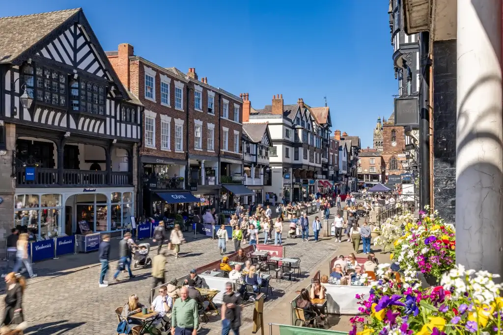 A bustling street scene filled with pedestrians and outdoor diners, framed by charming historic buildings under a clear blue sky.