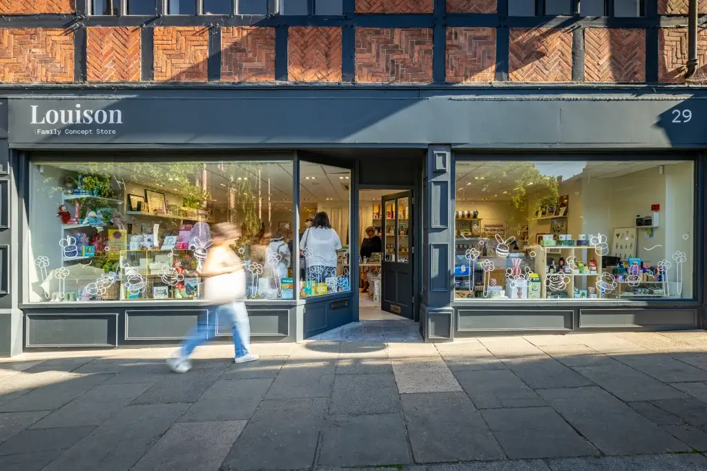 A family concept store named Louison, showcasing colorful goods behind a glass window, with a person walking by.