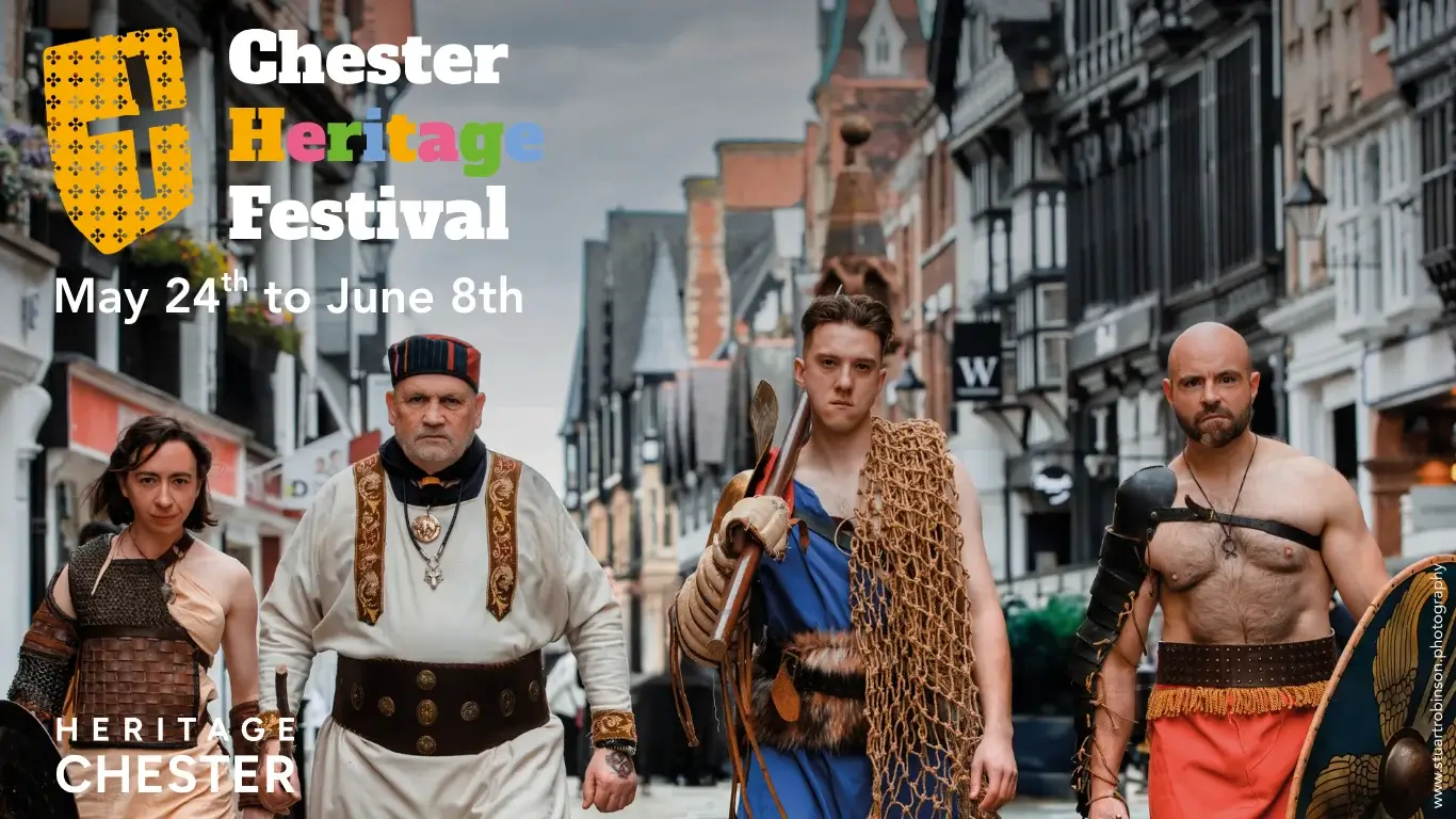 Four historical figures in traditional costumes walk down a charming, cobblestone street during the Chester Heritage Festival.