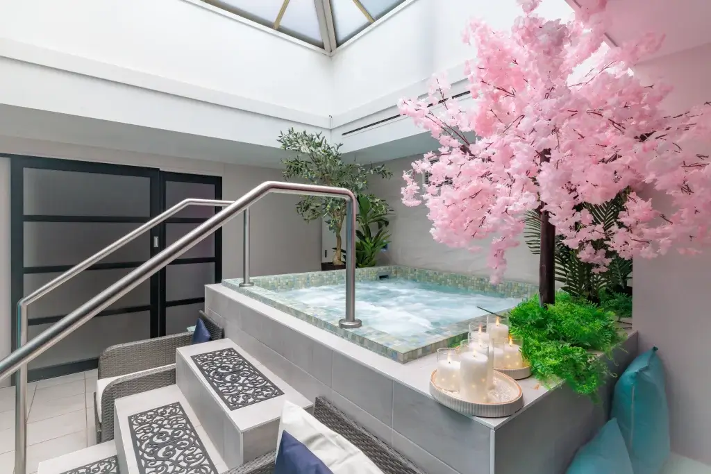 Indoor tiled hot tub with bubbling water, stainless handrail, pink cherry-blossom tree, lit candles and seating