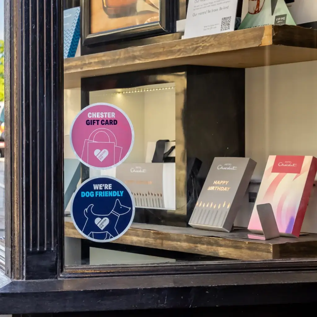 Store window features signs for a Chester gift card and dog-friendly policies, alongside displayed greeting cards.