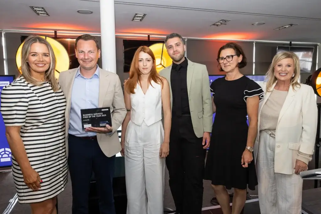 A group of six professionals gathered for an event, one holding a trophy labeled “Business Services Firm of the Year 2025".