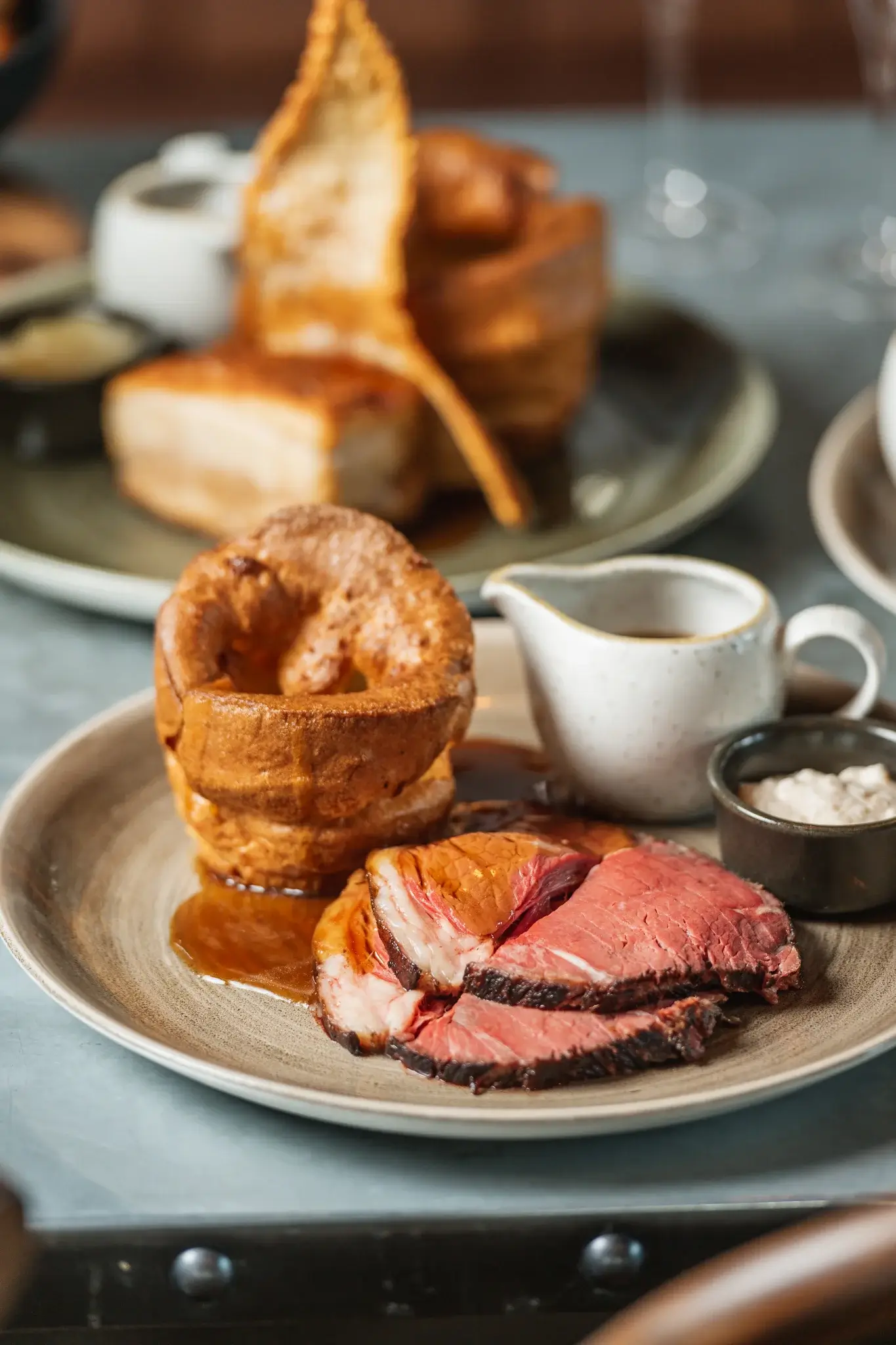 A plate featuring juicy slices of roast beef, a Yorkshire pudding, gravy, and dipping sauces, elegantly arranged on a rustic dish.