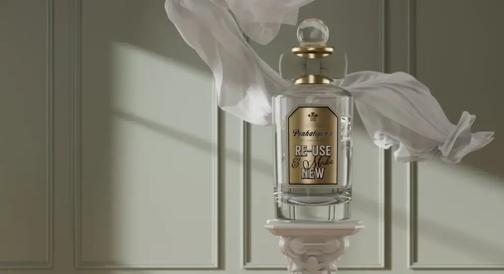 Glass perfume bottle labeled "Penhaligon's Re-Use & Make New," elegantly displayed against a muted green wall with flowing fabric.