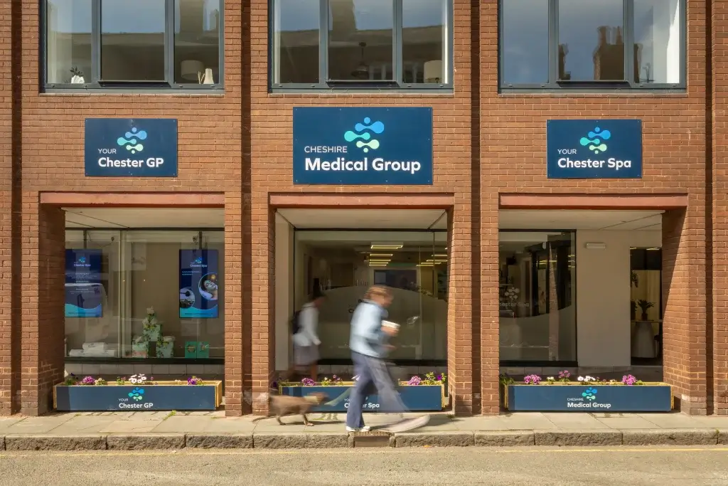 Exterior view of Cheshire Medical Group and Chester GP and Chester Spa signage, with a person walking a dog in front.