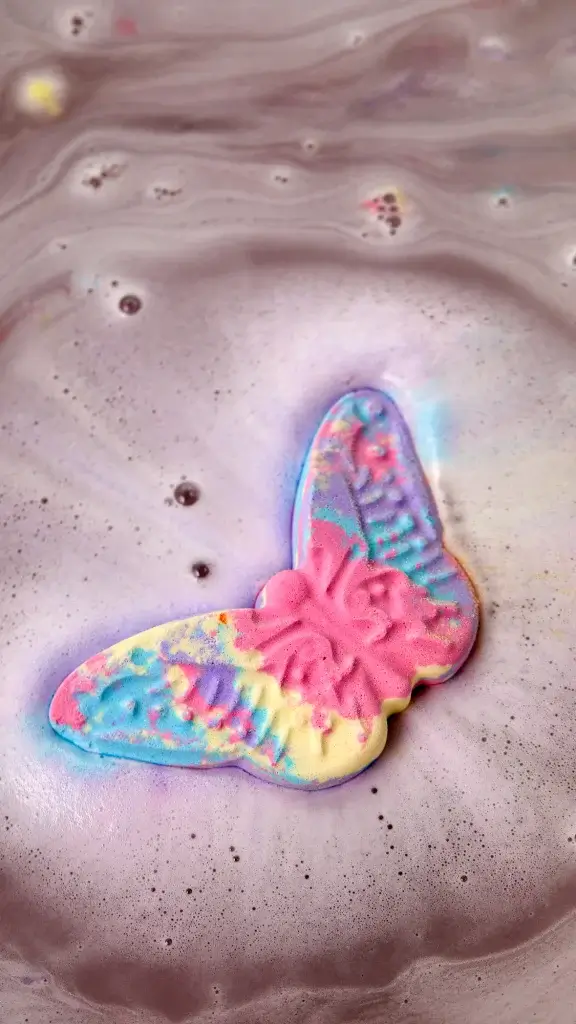 A colourful butterfly bath bomb sizzling in some water giving a rainbow of colour