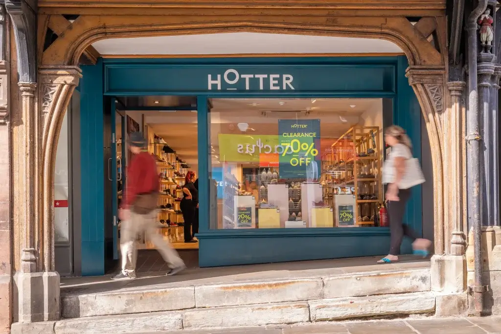 Front view of a Hotter shoe store featuring a sale sign for "up to 70% off," with pedestrians walking past the entrance.