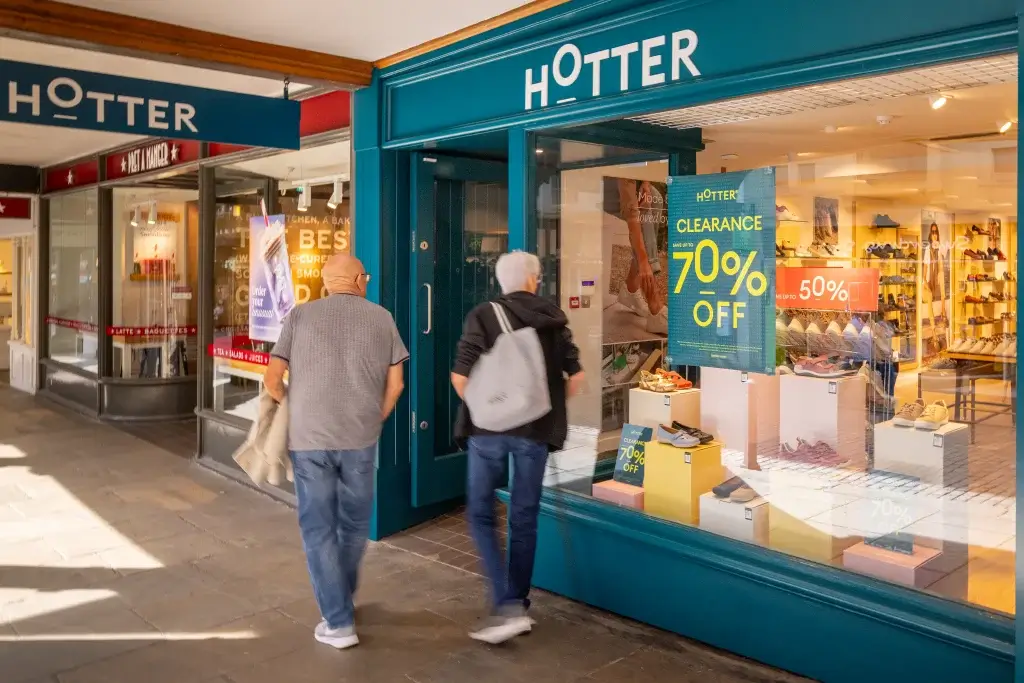 Two shoppers walk towards the HOTTER store, which advertises a 70% off sale, in a vibrant shopping arcade.