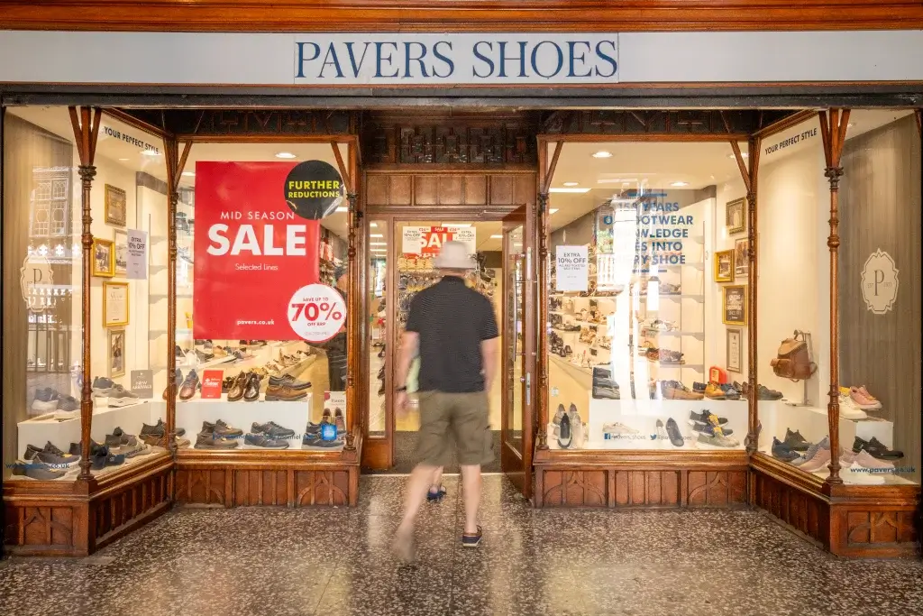 A man walks towards Pavers Shoes entrance, featuring a large "MID SEASON SALE" sign with discounts up to 70% displayed in the windows.