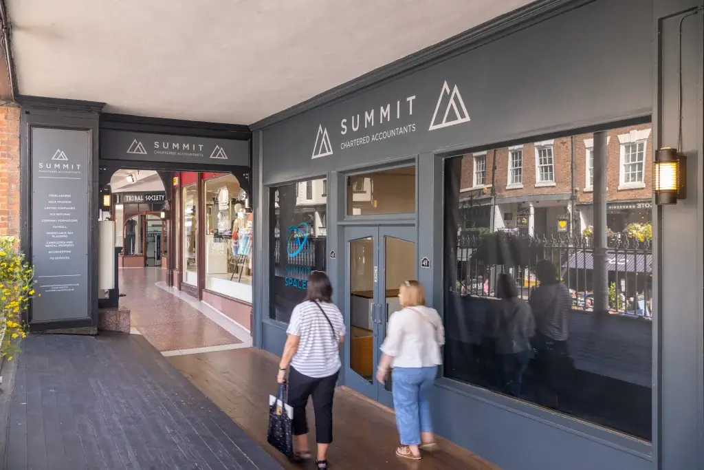 Two women walk past the entrance of Summit Chartered Accountants in a shopping arcade, surrounded by shops and greenery.