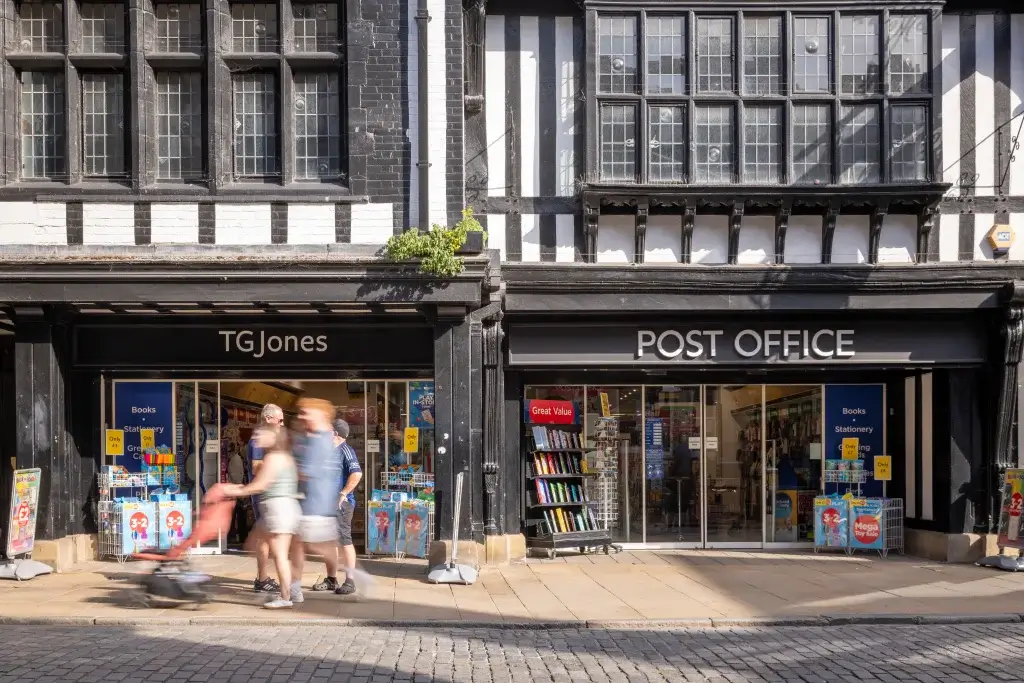 A busy street scene in front of TG Jones store, featuring people walking and browsing displayed merchandise, including books and toys.