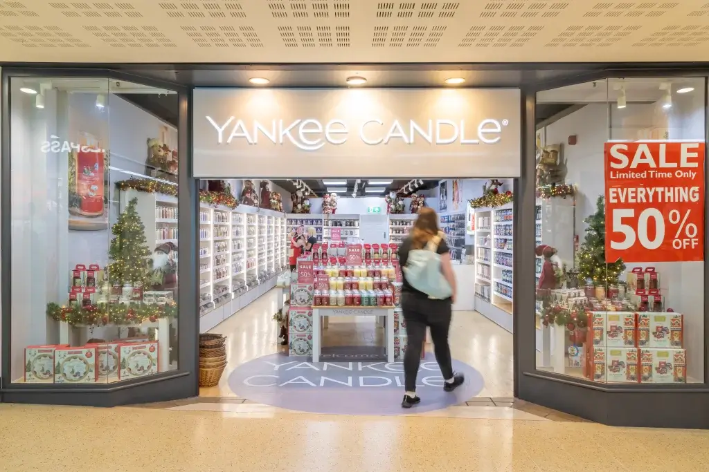 Entrance to a Yankee Candle store, showcasing colorful candles and festive decorations, with a customer browsing inside.