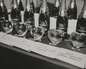 Line of champagne bottles and heart-shaped glass awards on a table with handwritten category cards