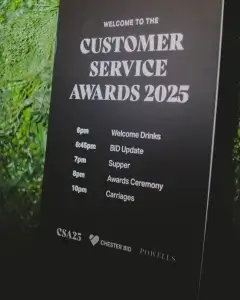 Black board reading Customer Service Awards 2025 with schedule from 6pm Welcome Drinks to 10pm Carriages set against green foliage.