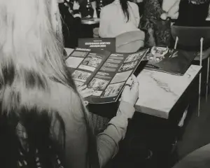 Person with long hair seen from behind reading a brochure at a marble-top table, visible headline Customer Service Awards 2025.