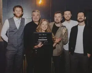 Group of six smiling people posing indoors, a woman at centre holding a framed Best Newcomer award for Salt House Tapas while a man beside her holds a small heart-shaped trophy.