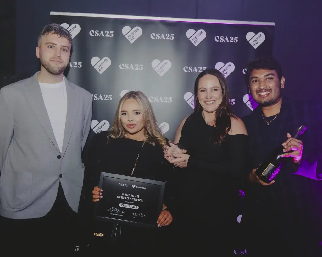 Four smiling people in front of a CSA25 backdrop holding an award plaque and a bottle of champagne.