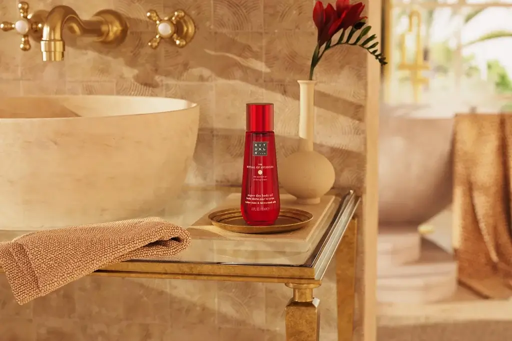 A bottle of super dry body oil by Rituals is displayed on a gold tray beside a textured towel and a decorative plant in a spa-like setting.