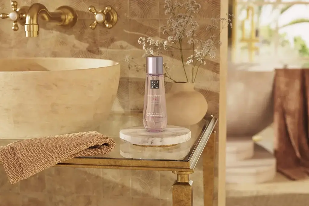 A bottle of super dry body oil by Rituals is displayed on a marble tray beside a textured towel and a decorative plant in a spa-like setting.