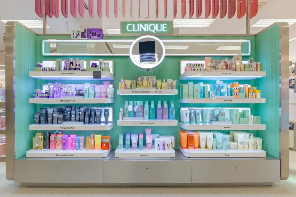 Clinique display with green backdrop, illuminated round mirror and colourful skincare on labelled shelves.