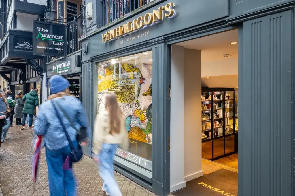 Penhaligon's shopfront with gold sign, colourful bird-and-butterfly window and blurred pedestrians on wet pavement.