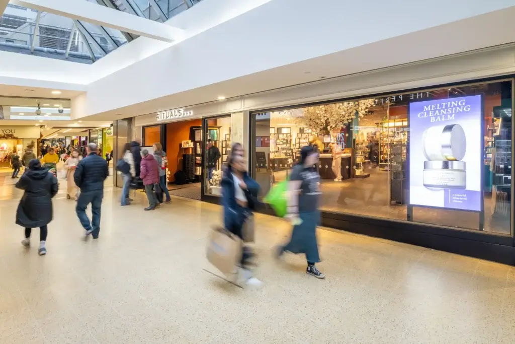 Shoppers walking past a Rituals store inside a bright mall, with a large Melting Cleansing Balm window ad and skylight above.