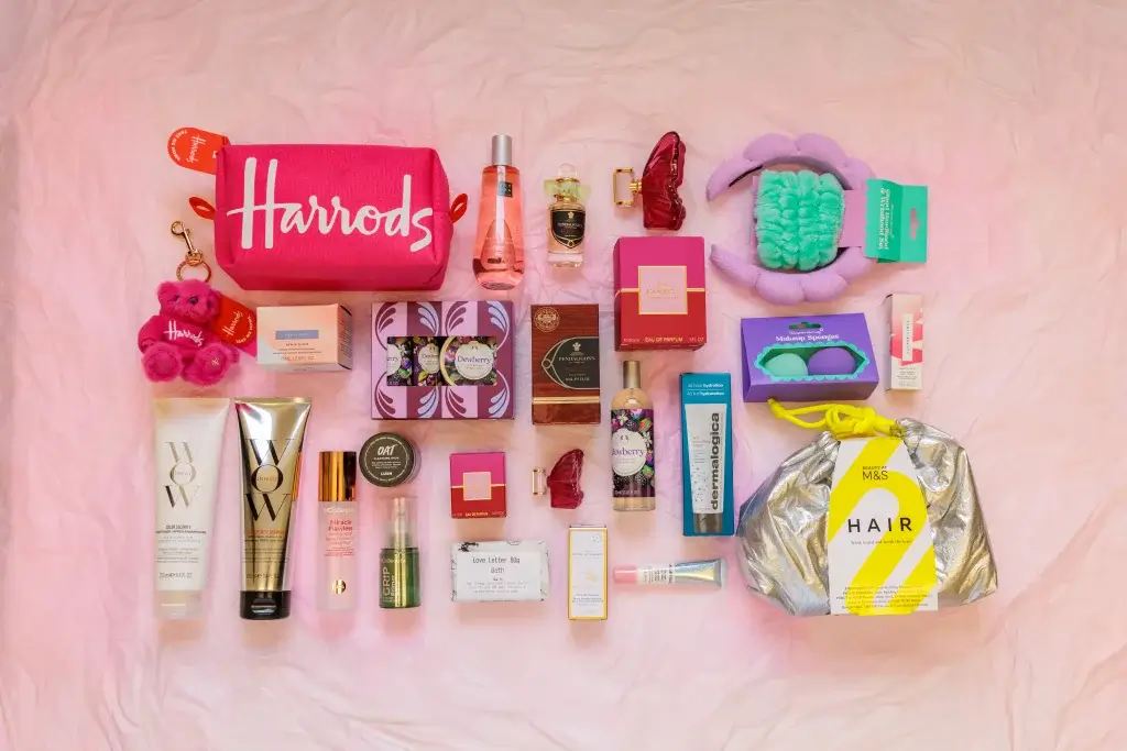 A flat lay of various beauty products, including skincare, haircare, and perfumes, alongside a pink Harrods pouch and accessories.