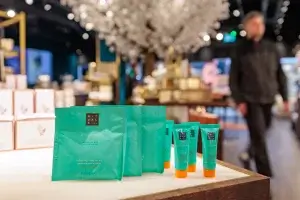 Turquoise Rituals body scrub sachets and small tubes with orange caps on a shop counter, blurred store interior behind