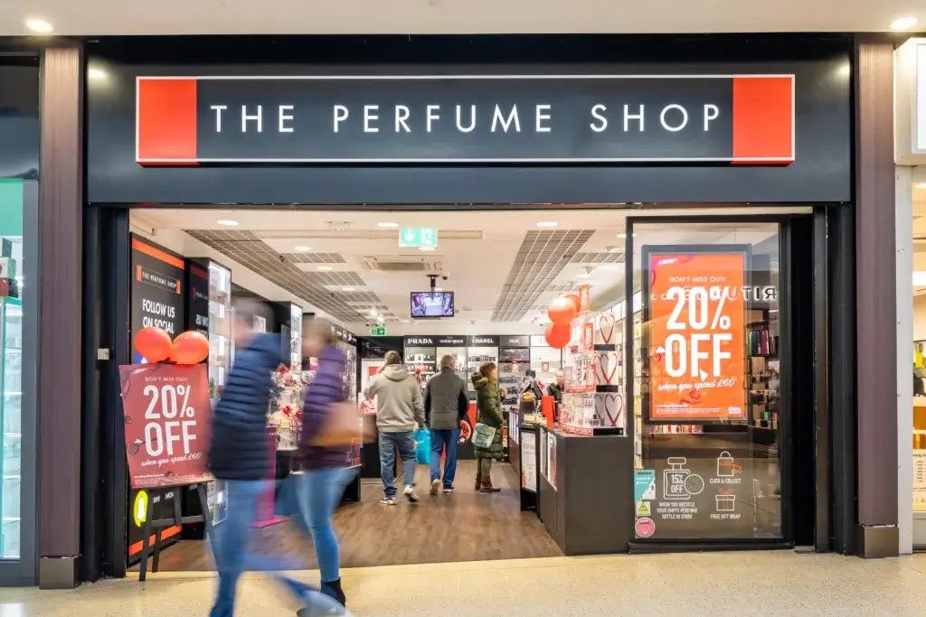 The Perfume Shop storefront with large black sign, 20% off posters, red balloons and blurred shoppers