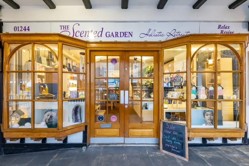 Wooden-fronted shop The Scented Garden with bay windows displaying products and a chalkboard sale sign.
