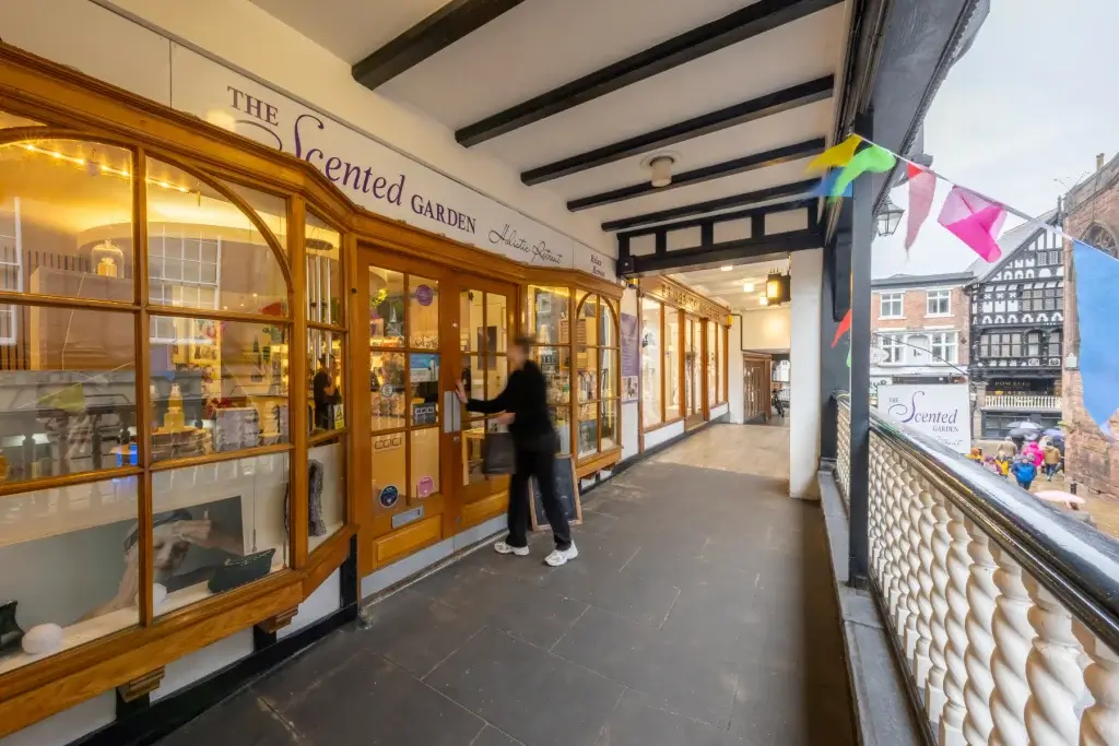 Person opening the wooden door of The Scented Garden on a covered balcony with colourful bunting and a Tudor building beyond.