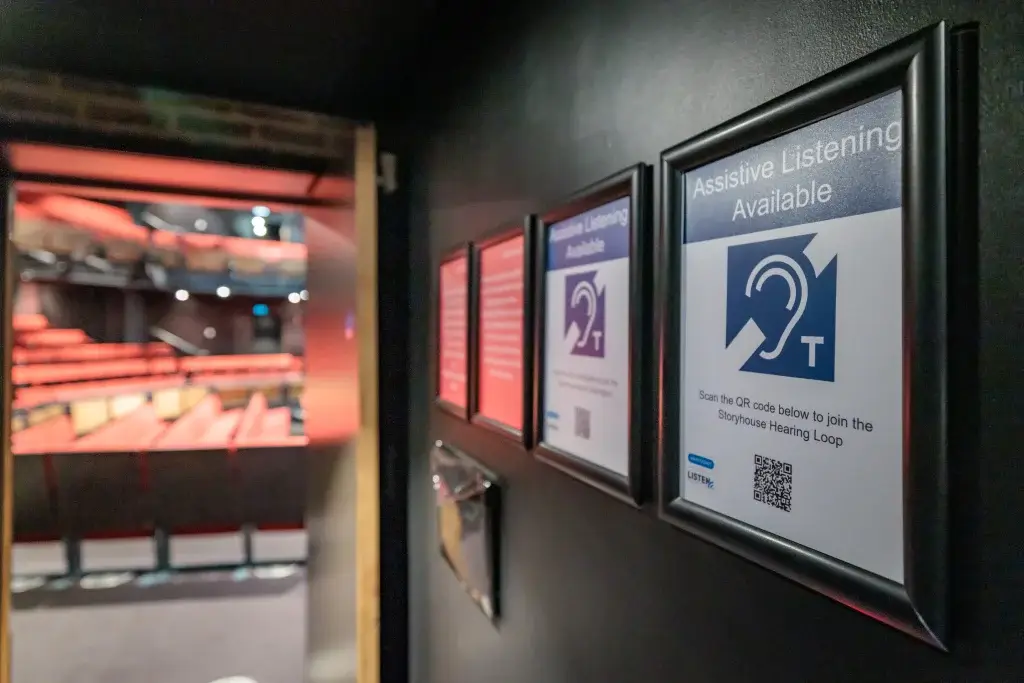 Posters on a wall showcasing Hearing Loop available with a theatre stage in the background